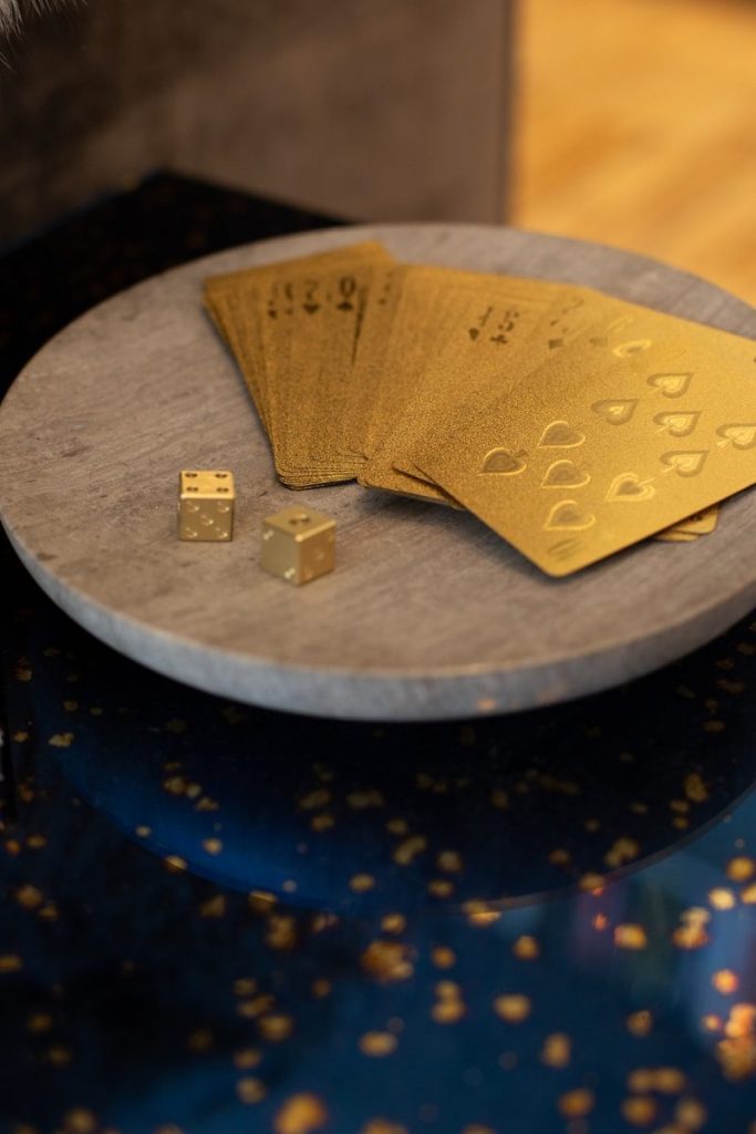 Luxury gold-colored playing cards and matching dice displayed on a round stone tray, symbolizing wealth and precious metals investing while illustrating Silver IRAs, what is self-directed IRA, what is IRA eligible gold, what is IRA approved gold, and what is a self-directed IRA account for retirement planning.